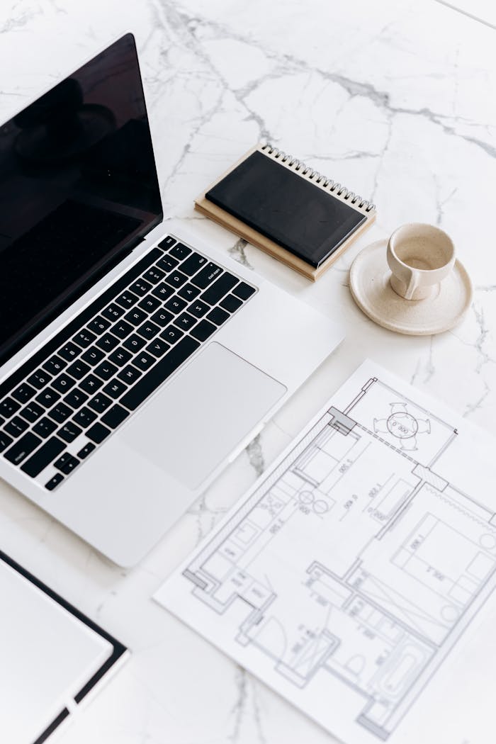 A clean, modern workspace with a laptop, blueprint, and coffee cup on a marble table.