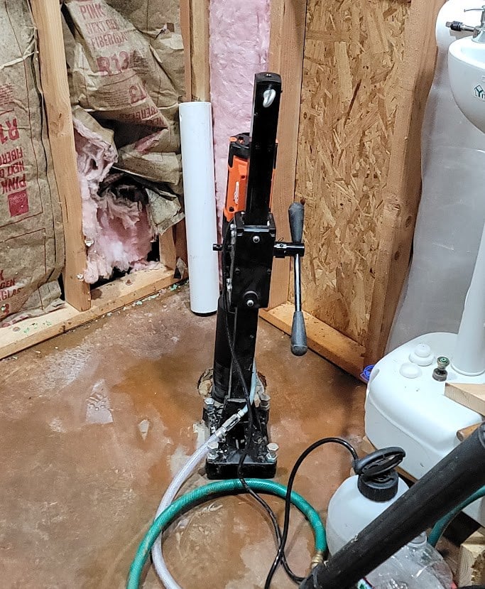 Core drill with a water line cutting a drain hole through a barndominium concrete slab inside a framed bathroom