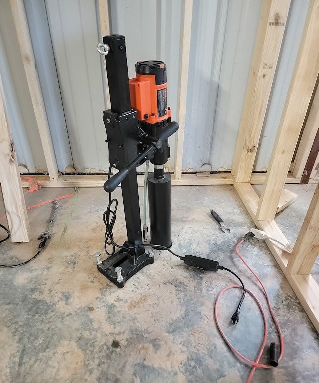 Core drill on a stand set up on a barndominium concrete slab between wall framing