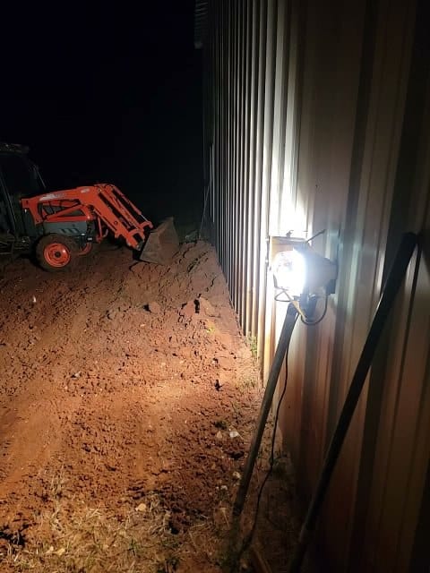 Tractor with a front loader beside a metal barndominium wall at night, lit by a work light